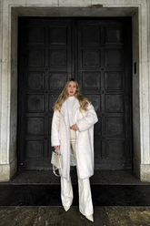 a lady wears a white lamb wool coat with a white turtle neck top